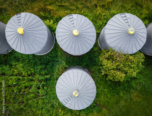 Four large silos are viewed from above, surrounded by lush greenery. The geometric symmetry of the roofs contrasts with the natural landscape.
