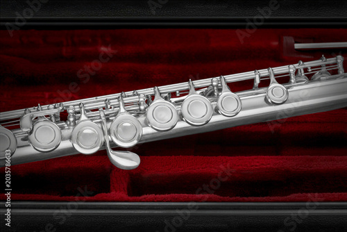 A detailed view of a silver flute resting in a plush red velvet case. The metallic surface contrasts beautifully against the deep red background.