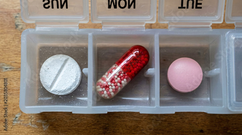 Top view of a medicine organizer showing precise daily prescription pills on wooden background.
