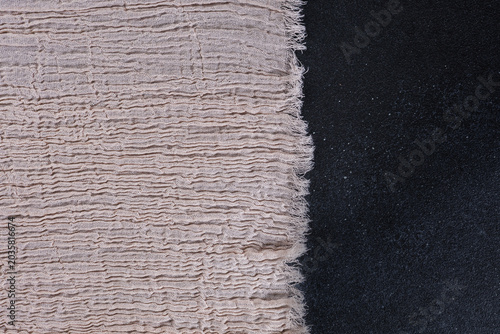 Beige crinkled muslin fabric with frayed raw edge on black textured background, soft cotton gauze textile border for branding mockup, boho design and handmade product presentation