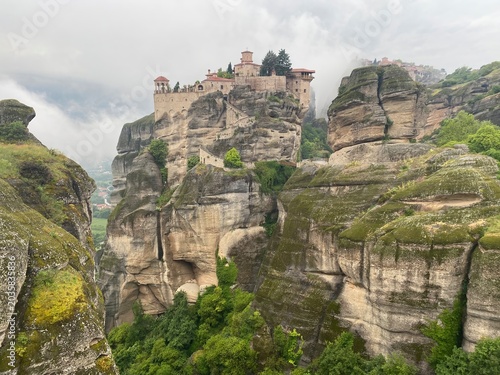 Stunning scenic view of the majestic Meteora rock formations and ancient monasteries enveloped in soft morning clouds and mist during a vibrant sunrise in Greece. Perfect for travel.