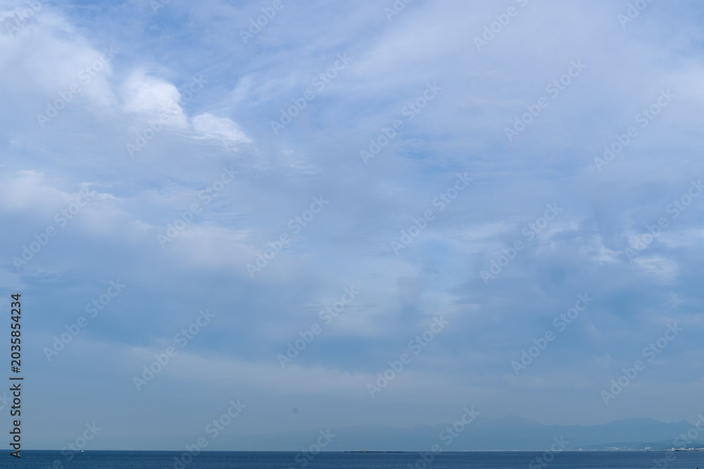 Obraz premium 穏やかな海辺と水平線の上に雲が広がる空の景色