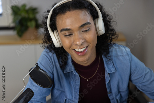 Non-binary person wearing denim shirt recording with microphone and white headphones at home studio