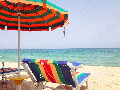 Schilderij op canvas A vibrant, striped beach umbrella casts shade over matching colorful sun lounger