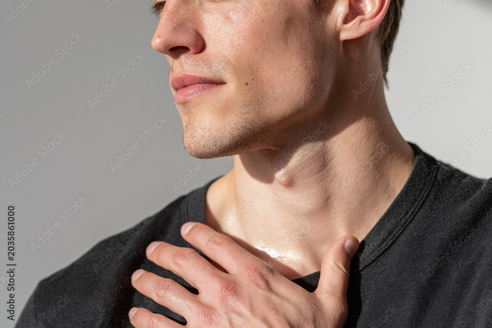 Fototapeta premium Young man hand on collarbone in sunlight, closeup skin texture, jawline, neck, casual gesture