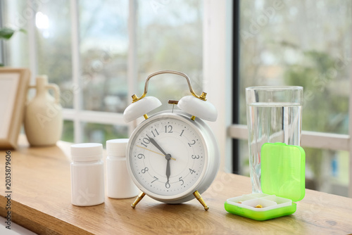 Obraz na płótnie Alarm clock with pills and glass of water on shelf in room