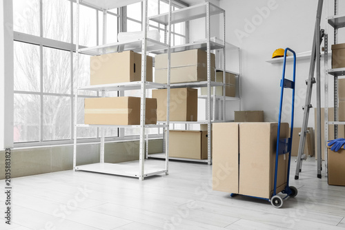 Foto Shelf units with cardboard boxes, trolley and stepladder in warehouse