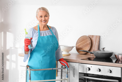Mature woman with walker, detergent and rag in kitchen