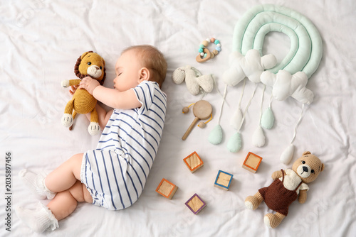 Cute little baby with toys sleeping on bed, top view
