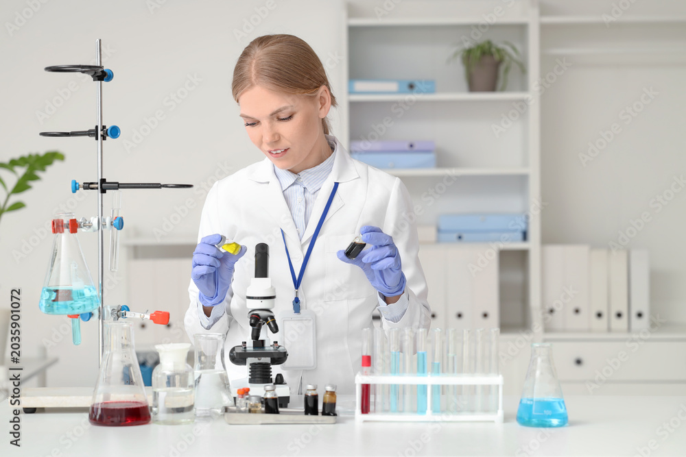 Fototapeta premium Female scientist with ampules and microscope at table in laboratory