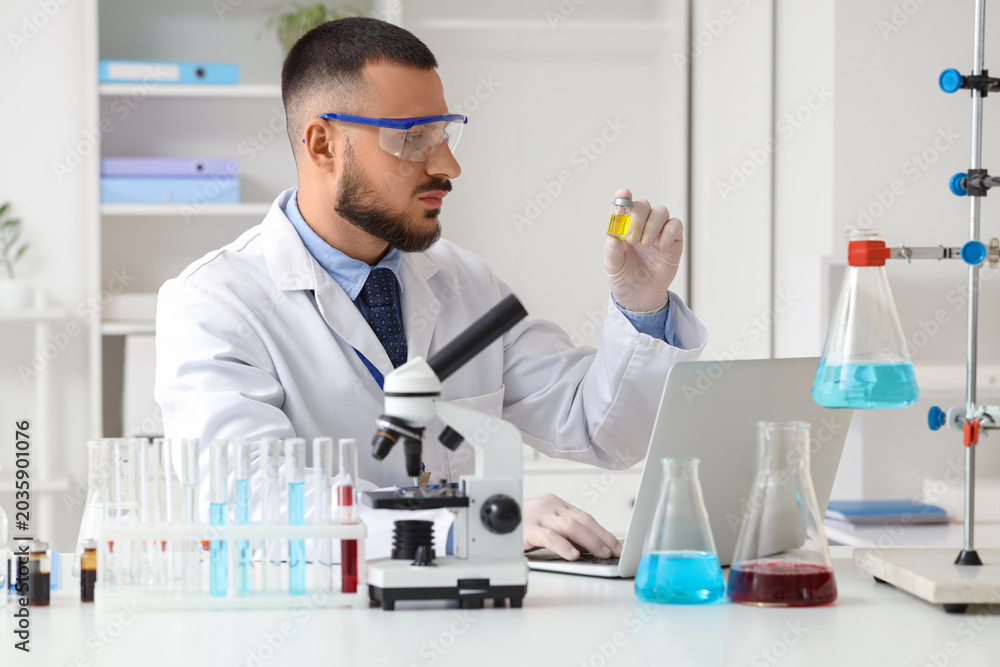Fototapeta premium Male scientist with ampule and laptop working in laboratory
