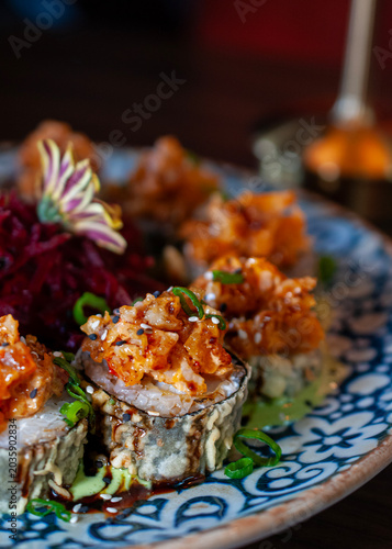 Sushi or seafood roll with cream, spices and sesame seeds on a decorative plate in a seafood restaurant in Mexico. Vertical.