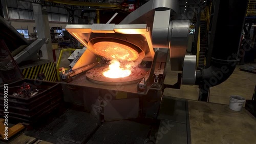 Cinematic industrial footage featuring molten metal pouring from a high-temperature furnace inside a modern manufacturing facility. Intense heat, glowing steel, sparks, heavy machinery, and industrial
