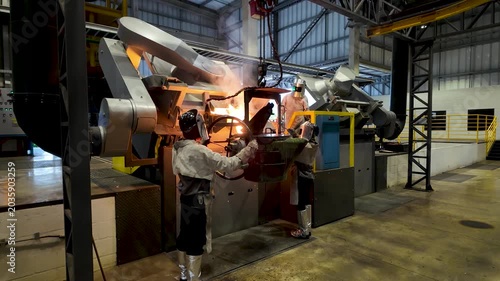 Cinematic industrial footage featuring molten metal pouring from a high-temperature furnace inside a modern manufacturing facility. Intense heat, glowing steel, sparks, heavy machinery, and industrial