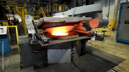 Cinematic industrial footage featuring molten metal pouring from a high-temperature furnace inside a modern manufacturing facility. Intense heat, glowing steel, sparks, heavy machinery, and industrial