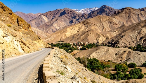 Winding Mountain Road Overlooking Arid Rocky Valley and Village Under Clear Blue Sky