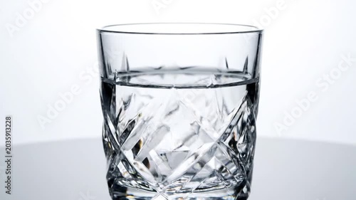 Cut crystal water glass on reflective surface.