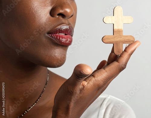 Close Up Black Woman Holding Wooden Cross Near Lips on Gray Background