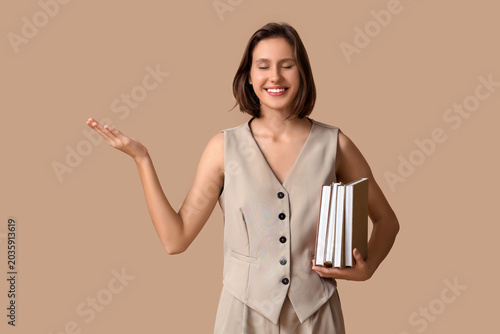 Smiling young woman holding books and presenting empty copy space with open p...