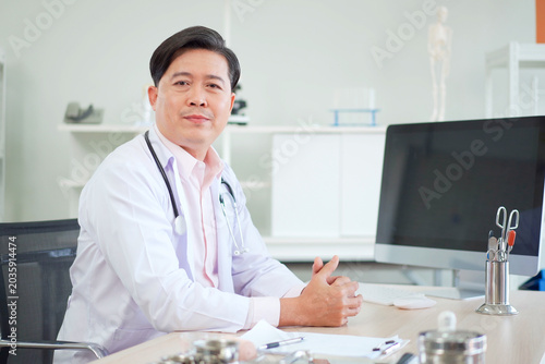 Quadro su tela Smiling asian doctor sitting in modern clinic office
