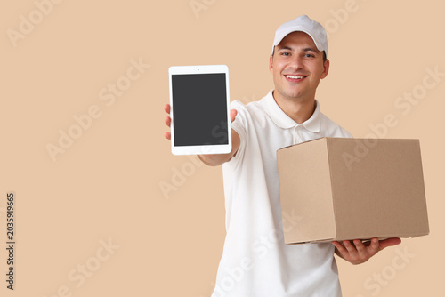 Delivery man with parcel box and tablet computer on beige background
