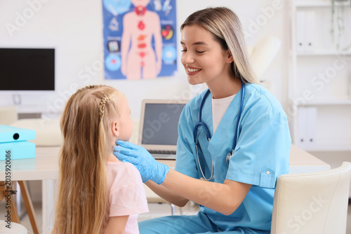 Female endocrinologist examining thyroid gland of little girl in clinic