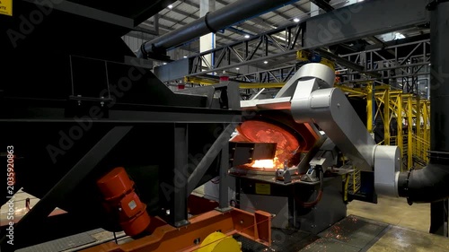Cinematic industrial footage featuring molten metal pouring from a high-temperature furnace inside a modern manufacturing facility. Intense heat, glowing steel, sparks, heavy machinery, and industrial
