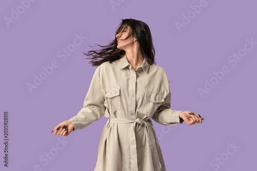 Tableau sur toile Beautiful young woman in stylish dress dancing on lilac background