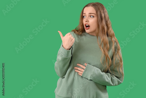 Foto Shocked young woman pointing at something on green background
