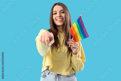 Foto Smiling young woman with LGBT flag pointing at viewer on blue background