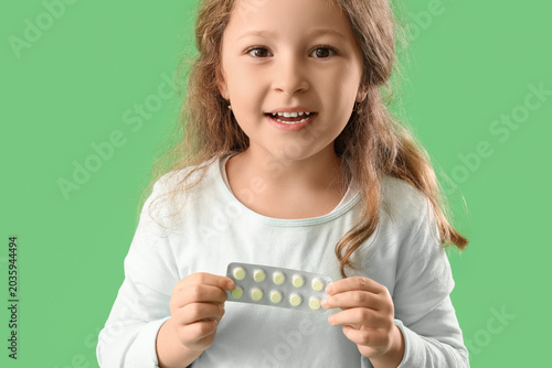 Little girl with pills on green background, closeup
