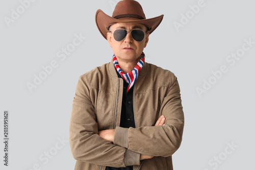 Mature cowboy in sunglasses on light background