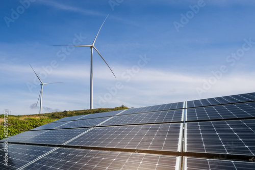 Solar panels and wind turbines generator in renewable energy farm with blue sky background for sustainable development.