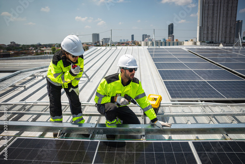 Professional solar panel technicians installing solar panels on commercial building roof, Team of engineers working on solar photovoltaic cell installation at industrial facility