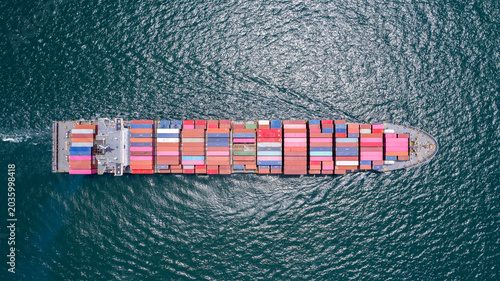 Canvas Print Container Ship in Open Sea: An overhead aerial view of a massive container ship carrying numerous colorful cargo containers sailing across the deep blue, wavy ocean