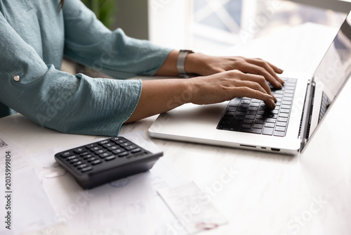 Tablou pe pânză Close up view of woman typing on laptop at desk with documents and calculator, f