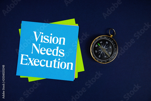 Vision Needs Execution text written on sticky note with compass on blue  background