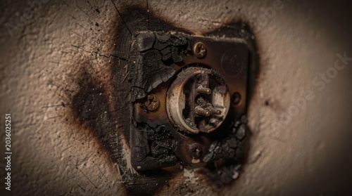 A close-up of a dangerously burnt and melted electrical socket on a scorched wall, illustrating the hazard of an electrical fire or short circuit.