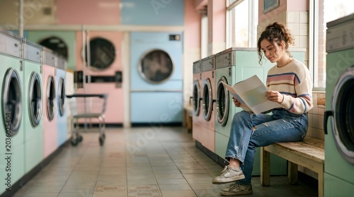 Young woman reading a magazine while waiting at a pastel laundromat