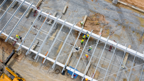 Cuadro en lienzo Industrial Construction Site: An aerial view of an industrial construction site shows workers in hard hats and high-visibility vests assembling a large metal structure