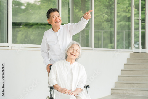 Quadro su tela A senior woman in a wheelchair and a senior man caring for her (image of a nursi
