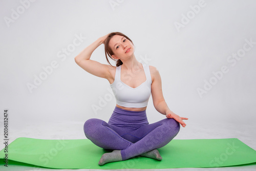 Full length portrait of young athletic woman sitting in lotus position on yoga mat isolated on white background.