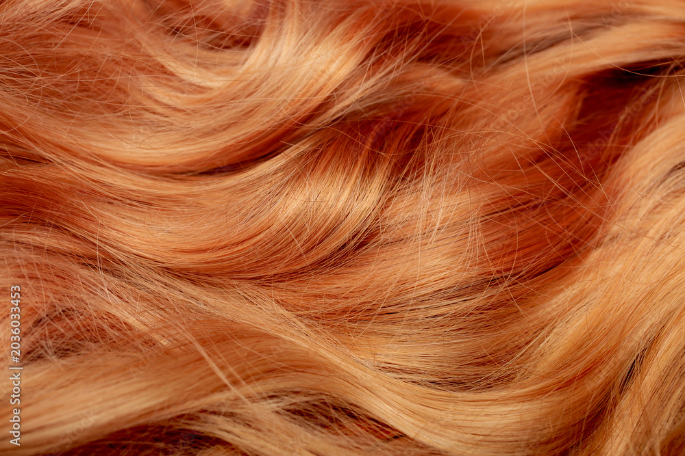 Naklejka premium Red hair close-up as a background. Women's long orange hair. Beautifully styled wavy shiny curls. Hair coloring bright shades. Hairdressing procedures, extension.