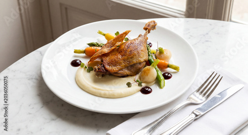 Classic French duck confit with crispy skin celeriac puree baby vegetables and cherry gastrique on white plate