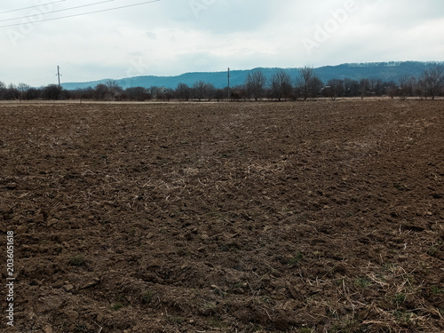 Freshly plowed farmland with loose soil and straw under a cloudy mountain sky.