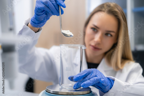 Weighting white powder samples with precision balances into beaker at pharmaceutical laboratory workstation