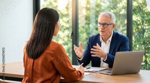 Serious mature businessman discussing project with young female colleague in modern office.