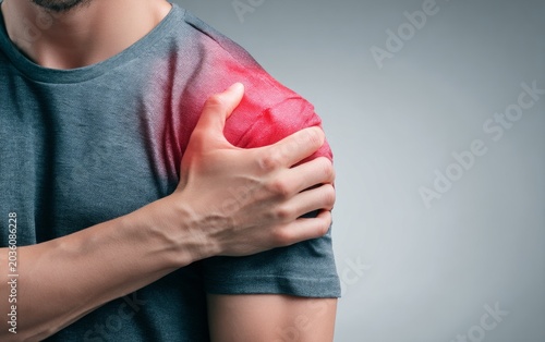 Man experiencing shoulder pain and discomfort, holding sore shoulder with hand