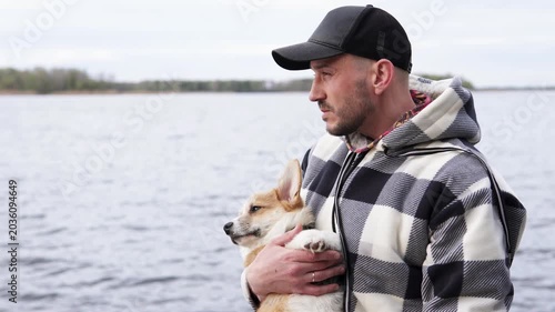 Young man enjoying walk with pembroke welsh corgi puppy by the river. Royal breed in trend, lifestyle and nature moment. Pets concept.