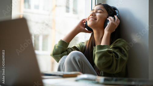 Overwhelmed remote student finding instant joyful release by escaping into an uplifting song away from her laptop screen.